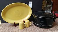 Front view of yellow Fiesta platter on stand with salt and pepper shakers in front and Hamilton Beach slow cooker beside them on counter.