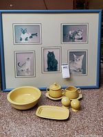Full lot including yellow Fiesta serving set and blue framed cat prints seen from front on flooring.