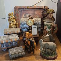 Front view showing tooled metal jewelry boxes of varying sizes, clock box with analog clock, carved wood and resin elephant figurines, and ceramic stein with lid.