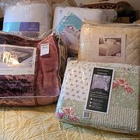 Photo shows overall lot with king size bedspreads, plush fleece blanket, queen and king mattress pads in packaging.