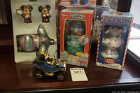 Overview photo of the four items on wooden surface: Mickey Mouse tin car, Dumbo coin bank, Rudolph bobblehead, and Dumbo salt and pepper set in original packaging