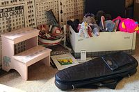 Photo showing mini steel drum, drumsticks, pink elephant stepstool, box of plush toys, and black instrument case in front of chord posters