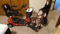 Full view of red motorized scooter and folding rollator wheelchair side by side