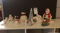 Assorted unwrapped Snowbabies and Angel Cloud figurines on shelf including Santa, polar bear, snowman, Christmas tree and toy train