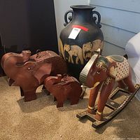 Full lot photo showing tall black ceramic urn, reddish-brown metal elephants, and large painted wooden rocking elephant figurine.