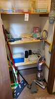 Photo showing Shark stick vacuum leaning in corner plus shelves holding multiple stacks of plastic snapware containers with lids in pink, yellow, blue and clear colors. Mop, dusters, and black cylindrical containers also visible.
