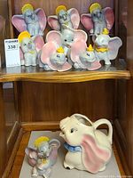 Full set including nine elephant figurines on shelf and Dumbo pitcher on lower shelf.