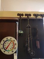 Photo showing plastic wall thermometer and different elephant-themed wind chimes and hooks hanging on dark wall.
