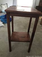 Full front view of wooden accent table on carpet showing overall shape, legs, shelf, and tabletop.