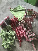 Wide view showing multiple wired ribbon bows in green polka dot, red polka dot, and red/white stripes along with packaged small ball ornaments and a fabric tree skirt.