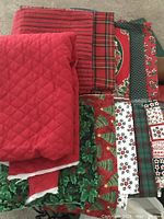 Top view of various assorted Christmas patterned fabrics including red quilted fabric, plaid, holly, candy cane, and tree patterns.
