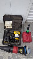 Photo of the DeWalt drill in its case with charger and manual, beside the red gas can and funnels on the floor.