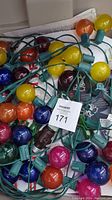 Close-up of multicolored globe Christmas light bulbs tangled with green wiring.