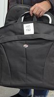 Close-up view of the American Tourister black garment bag held by a hand, showing the logo and bag structure.