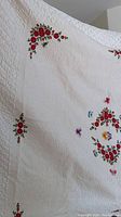 White satin bedspread with red rose embroidery and butterfly details, showing floral corner and central design.