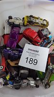 Photo showing multiple Matchbox cars piled in a container with a visible auction tag.
