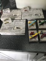Top down photo of 3 miniature vintage car models in original display boxes along with 4 miniature airplane models, some still in boxes. Cars display early 20th-century vintage style. Airplanes include several biplanes and a monoplane in various colors with star insignia.