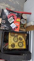Top view of a plastic bin containing assorted metal grinder brushes and gears, along with other metal parts and a red tool boxed labeled Skil.