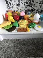 Plastic toy play food and blue plastic toy dishware items arranged on a white surface, showing a variety of toys with food item details and dishware quantity.