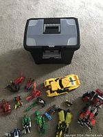 File-style black and gray plastic storage box containing Transformers and other small figurines placed on carpet.