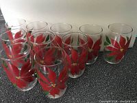 Front view of ten clear glass tumblers arranged showing hand painted red poinsettia flower design