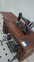 Side angle showing full view of Singer treadle sewing machine mounted in oak wood cabinet with drawers and treadle base.