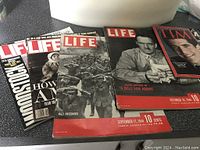 Photo showing vintage Life magazines with WWII and Nazi prisoners themed covers and one Time magazine with a portrait cover.