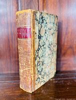 Front spine view showing aged leather binding with red label and marbled cover on the side.