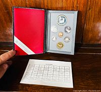 Folder open showing all seven coins in gray foam insert and red interior cover