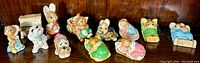 Side view of eleven Pendelfin collectible figurines arranged on a wooden surface, featuring bunnies, dogs, and cats in various whimsical poses and props.