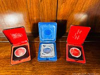 Three Canadian centennial silver dollars in their presentation cases arranged side by side on wooden surface