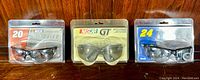 Three pairs of factory-sealed NASCAR branded protective eyewear side-by-side on wooden surface