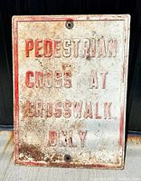 Front view of old metal embossed pedestrian sign with visible wear, rust spots, and faded red and white paint.