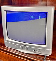 Silver RCA 13V420T CRT television powered on showing screen with TV channel 9 indication in green text on blue background.