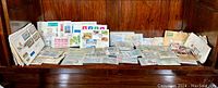 Wide view of various stamp packets, envelopes, and loose stamps arranged on a wooden bench.