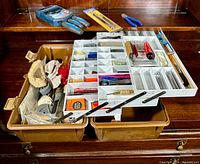 Open plastic toolbox with multiple white compartments showing removable trays with small tools and hardware items inside, displayed on wooden dresser.