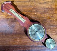 Top view of the wooden weather instrument showing the round barometer dial and the smaller hygrometer dial on the handle.