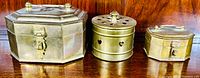 Set of three solid brass boxes including two octagonal lockable boxes and one round potpourri box with pierced lid on a wooden surface.