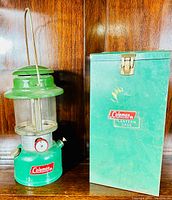 Green Coleman No. 4 propane lantern alongside original green metal travel case, showing front views.