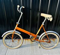 Side view of entire orange KENT folding bicycle with white seat and tires, showing the folded frame and both fenders.