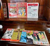 Photo showing full spread of eight vintage magazines displayed on a wooden surface: five LIFE magazines, one Holly Leaves, and two Illustrated London News magazines.
