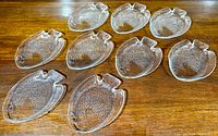 Set of nine clear glass plates shaped and detailed like fish laid out on wood table
