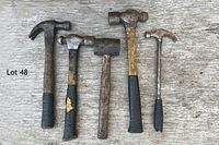 Photo shows five assorted hammers laid out on a wooden surface, all showing heavy use with rust and worn handles.