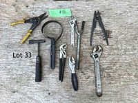 Well-used assortment of hand tools arranged on wooden surface, showing different types of hand tools including wrenches, pliers, and clamps.