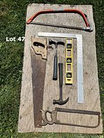Photo showing all tools arranged on wooden board—two saws, two hammers, spirit level, and two L-squares