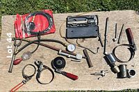Various assorted vintage automotive and mechanical tools laid out on a wooden surface including hose clamps, gauges, hand tools and connectors