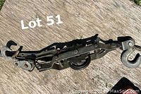 Metal ratchet lever tool with hooks and gears shown on wooden surface, visibly worn and aged.