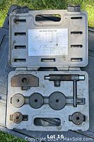 Open black plastic carrying case showing disk brake caliper tool components including threaded piston retractor tool and adapter plates on molded slots with instruction label inside lid.