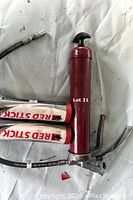 Red grease gun with hose and lever and two Red Stick 2 cartridges