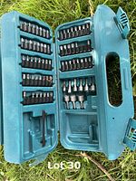 Open blue case displaying organized Makita drill and screwdriver bits in molded compartments, mostly full with some missing bits.